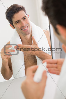Man with reflection putting moisturizer on face