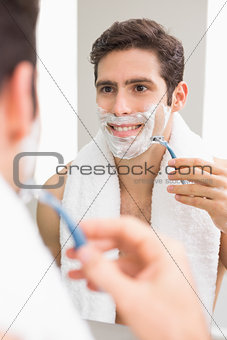 Handsome young man with reflection shaving in bathroom