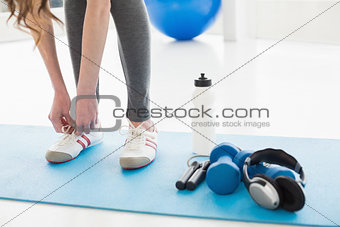 Woman tying shoes with sporty equipment on floor