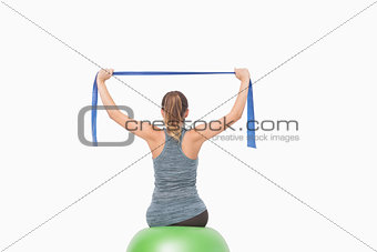 Ponytailed woman training using a resistance band sitting on a fitness ball