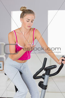 Sporty blonde training on exercise bike listening to music