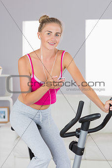 Sporty smiling blonde training on exercise bike listening to music