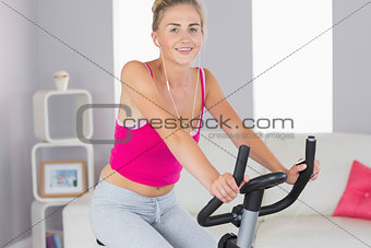 Sporty cheerful blonde training on exercise bike listening to music