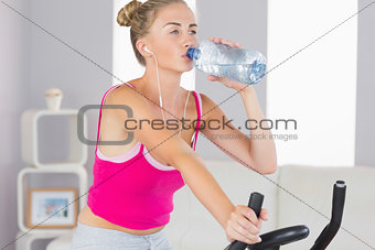 Sporty focused blonde training on exercise bike drinking water