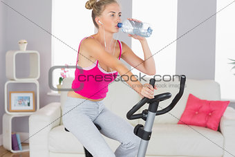 Sporty determined blonde training on exercise bike drinking water