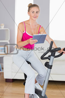 Sporty smiling blonde training on exercise bike using tablet