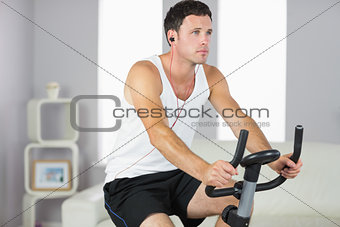 Attractive sporty man exercising on bike and listening to music
