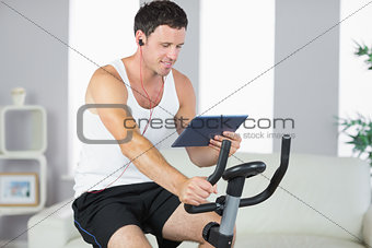 Smiling sporty man exercising on bike and using tablet