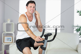 Cheerful sporty man exercising on bike and phoning