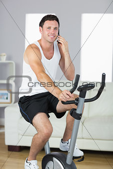 Content sporty man exercising on bike and phoning