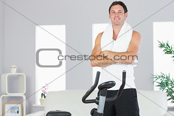 Cheerful sporty man standing next to exercise bike cross armed