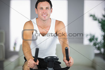 Attractive fit man exercising on bike smiling at camera