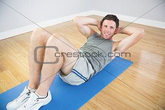 Smiling sporty man doing sit ups on blue mat