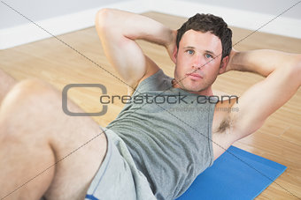 Calm sporty man doing sit ups on blue mat