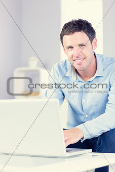 Cmiling casual man looking at camera using laptop