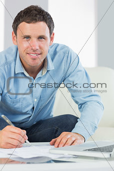 Happy casual man writing on sheets paying bills