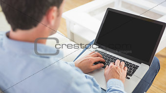 Looking over shoulder of casual man using laptop