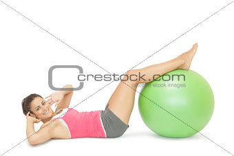 Smiling sporty brunette doing sit ups with exercise ball