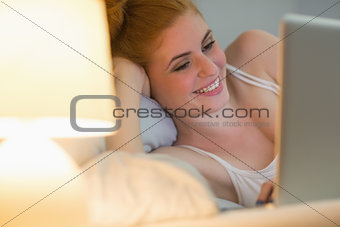 Smiling redhead lying on her bed using laptop