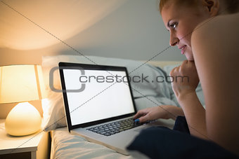 Young redhead lying on her bed using laptop