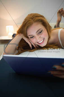 Attractive redhead using digital tablet lying on her bed