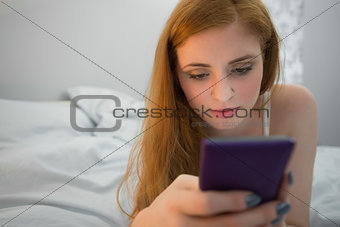 Happy redhead lying on bed sending a text