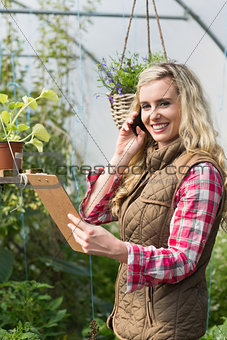 Phoning woman holding a clipboard in her green house