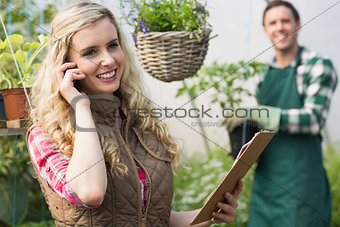 Smiling blonde woman phoning in a green house