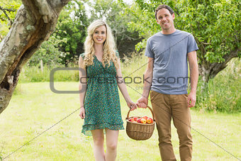 Smiling couple carrying a basket of apples
