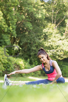 Sporty woman stretching her leg and smiling at camera