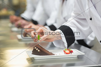 Team of chefs in a row garnishing dessert plates
