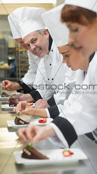 Team of chefs in a row garnishing dessert plates one smiling at camera