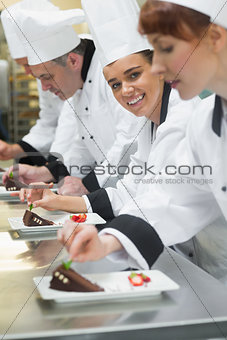 Team of chefs in a row garnishing dessert plates one girl smiling at camera
