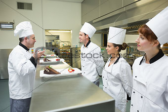 Three chefs presenting their dessert plates to the head chef