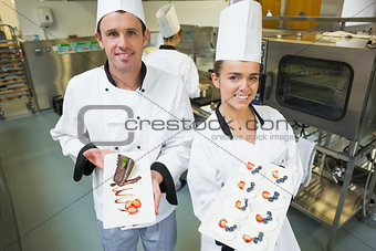 Two smiling chefs presenting dessert plates