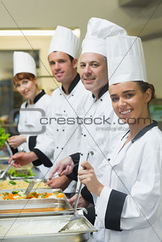 Four chefs working at serving trays smiling at camera