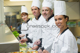 Four chefs smiling at camera while working at serving trays