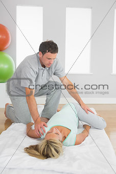 Physiotherapist examining patients hips on a mat on the floor
