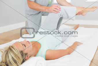 Physiotherapist checking patients leg on a mat on the floor