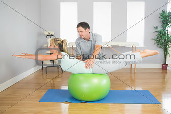 Physiotherapist helping patient doing exercise with exercise ball