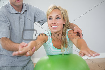 Physiotherapist correcting patient doing exercise on exercise ball