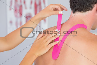 Physiotherapist putting on pink kinesio tape on male patients neck