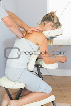 Masseur treating clients shoulder in massage chair