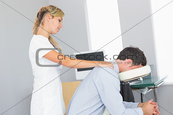 Masseuse treating shoulders of client in massage chair