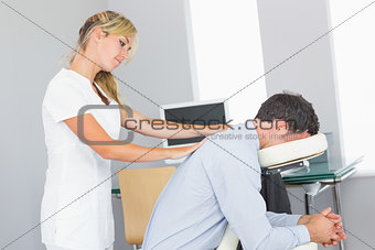 Masseuse treating clients shoulder in massage chair
