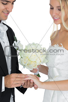 Smiling bridegroom putting the wedding ring on his wifes finger