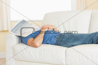 Casual man sleeping on couch with newspaper on his head