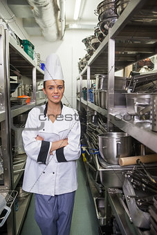 Young smiling chef standing arms crossed between shelves