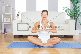 Front view of meditating slim woman sitting in lotus position on exercise mat