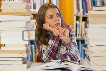 Serious pretty student sitting between piles of books